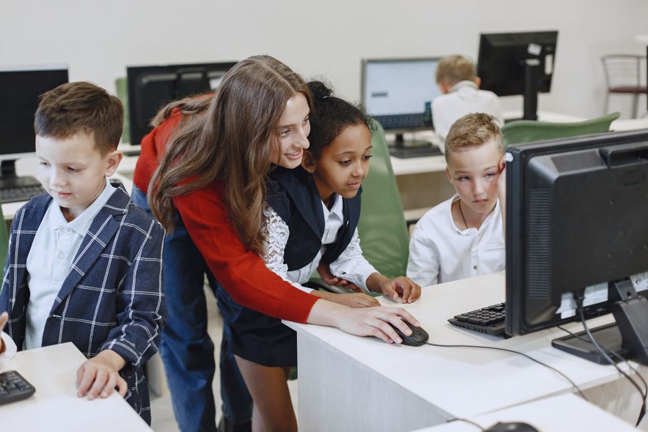 Teacher engaging with diverse children in a technology lesson using computers