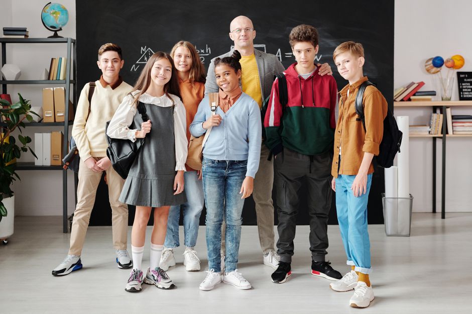 Group of diverse teenagers posing with their teacher in a modern classroom