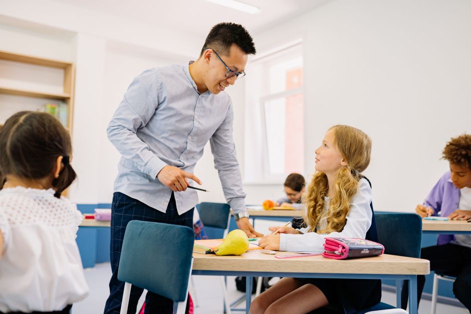A male teacher interacting with diverse students in a bright classroom setting, promoting active learning.