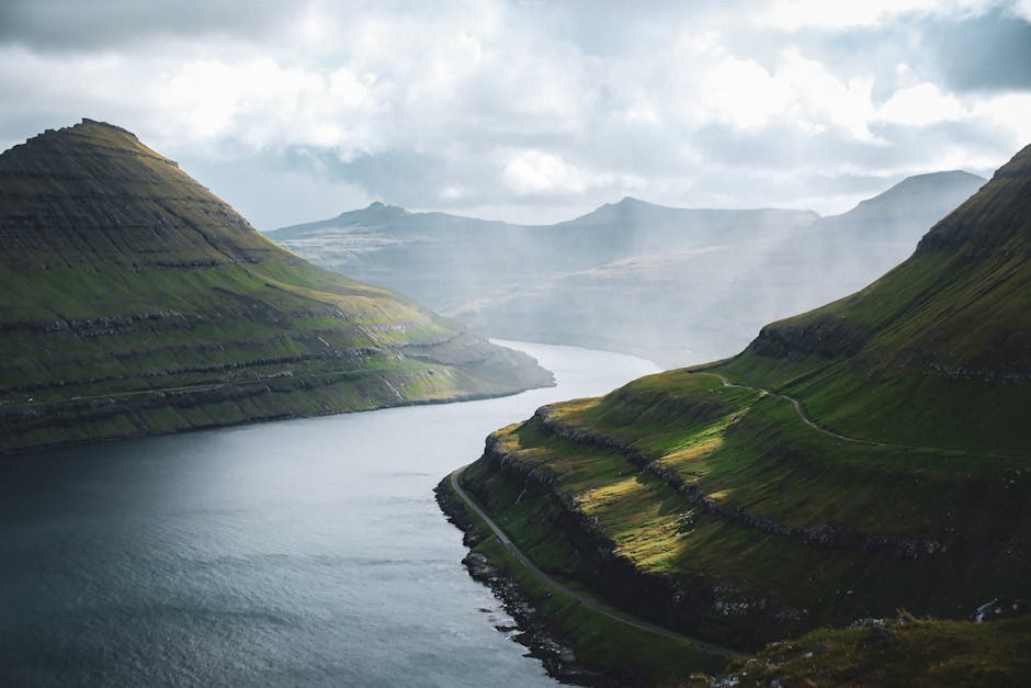 Beautiful view of a serene fjord surrounded by lush, green hills under a moody sky in the Faroe Islands